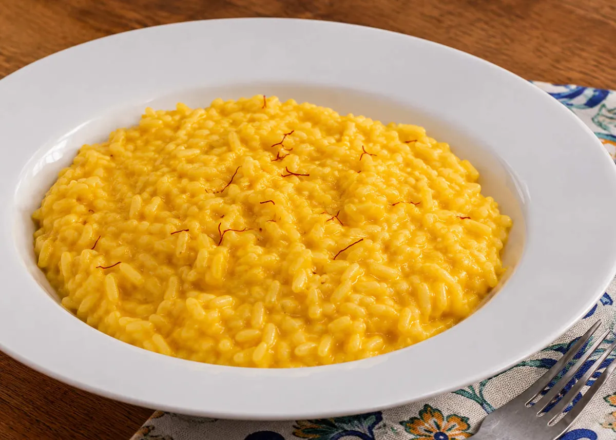 Golden saffron risotto alla milanese in a wide white bowl, with a few red saffron threads on top