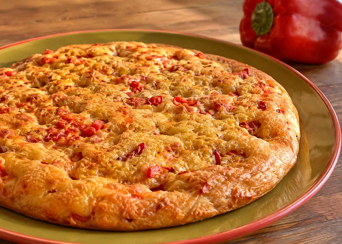 Golden bell pepper schiacciata flatbread on a large plate, dotted with pieces of red pepper