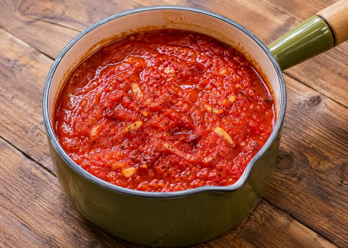 Saucepan of bright red spicy arrabbiata tomato sauce on a wooden table