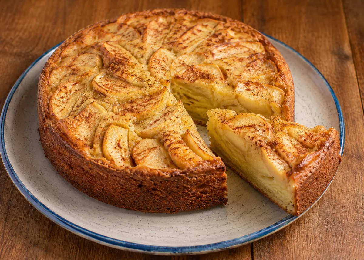 Vegan apple cake on a blue-rimmed plate with a slice cut out, topped with thin golden apple slices