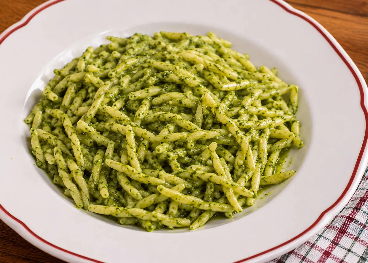 Trofie pasta coated in bright green basil pesto on a white plate with a red rim