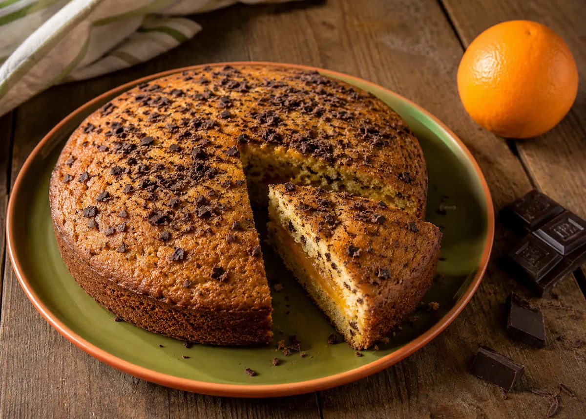 Eggless vegan orange marmalade and chocolate chip cake with a slice cut out and a whole orange beside it