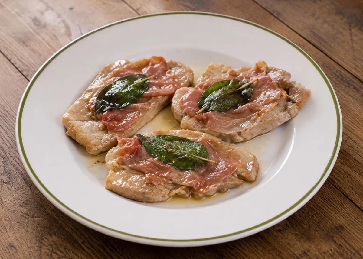 Saltimbocca alla romana: veal cutlets wrapped in prosciutto and topped with sage leaves on a white plate